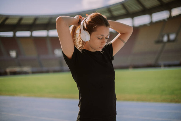 A beautiful girl is tying her hair. She is about to jog early in the morning with headphones on - Photo, Image