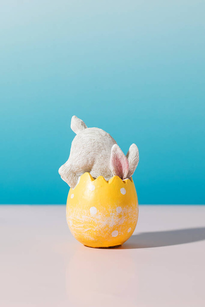 A white rabbit in an Easter egg on a blue background with shadows. The concept of a happy Easter. - Foto, Bild