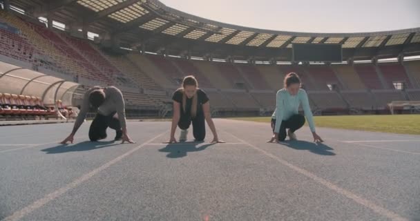 Tres jóvenes compiten en la pista de atletismo en un estadio, movimiento de cámara dolly - Metraje, vídeo