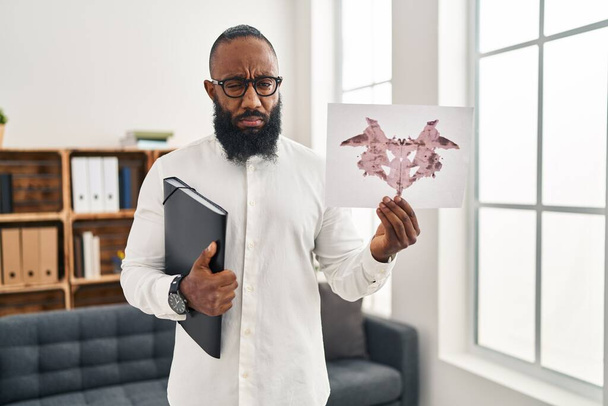 African american man working with rorschach test at psychology clinic skeptic and nervous, frowning upset because of problem. negative person.  - Photo, Image