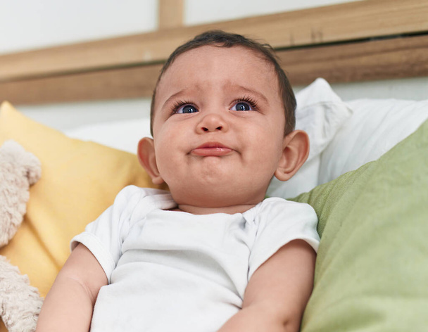 Adorabile bambino ispanico seduto sul letto a piangere in camera da letto - Foto, immagini