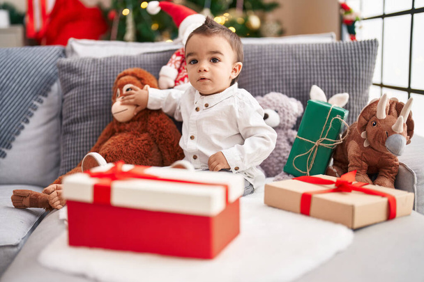 Adorabile bambino ispanico seduto sul divano vicino all'albero di Natale a casa - Foto, immagini