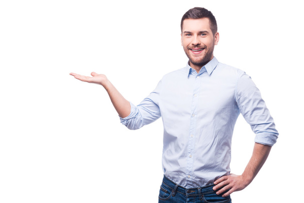Presenting new project. Handsome young man in shirt looking at camera and holding copy space while standing against white background - Фото, зображення