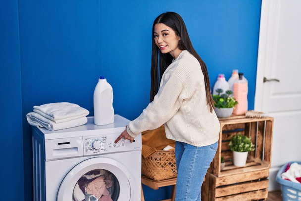 Young beautiful hispanic woman smiling confident washing clothes at laundry room - Foto, Imagem