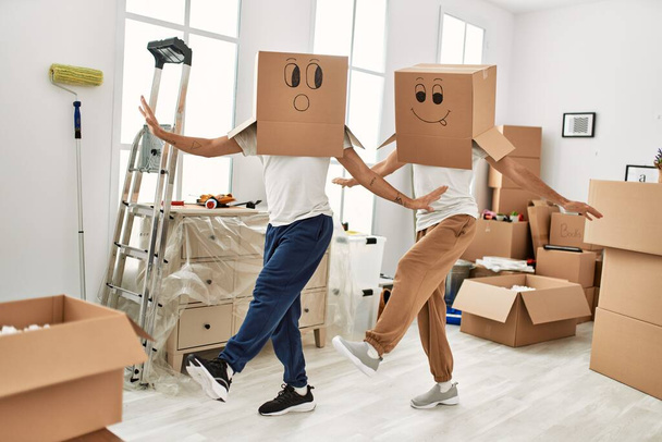 Due uomini ispanici coppia giocando con scatole di cartone divertenti sulla testa a nuova casa - Foto, immagini