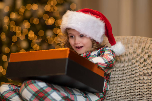 Meglepetés gyerek, karácsonyi ajándékokat nyit. Télapó piros sapkás gyerek karácsonyi ajándékkal. Karácsony és újév koncepció - Fotó, kép