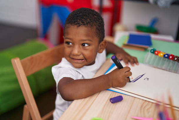 Африканский американец, дошкольник, сидит за столом и рисует на блокноте в детском саду - Фото, изображение