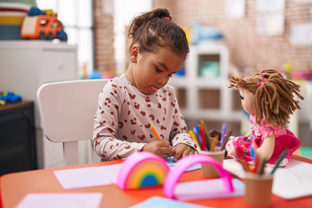 Симпатичная латиноамериканка, сидящая за столом и рисующая на бумаге в детском саду. - Фото, изображение