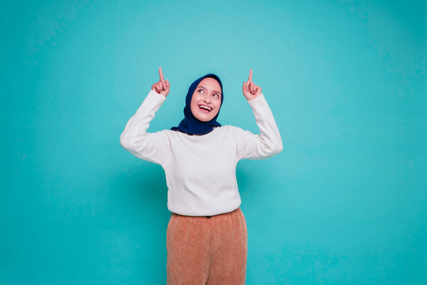 Izgalmas ázsiai nő fehér ingben és hidzsáb mutatva a fénymásoló hely rajta, elszigetelt kék háttér - Fotó, kép