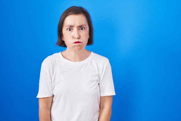 Middle age hispanic woman standing over blue background puffing cheeks with funny face. mouth inflated with air, crazy expression.  - Foto, Imagen