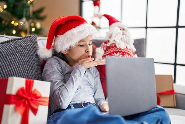 Adorable chinese girl having video call sitting on sofa by christmas tree at home - 写真・画像