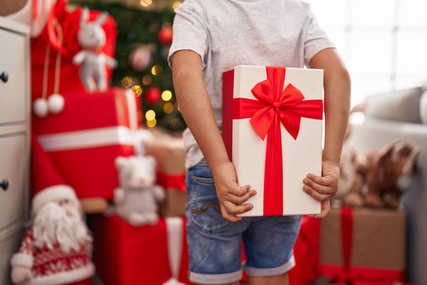 Adorable toddler holding gift standing by christmas tree at home - Foto, immagini