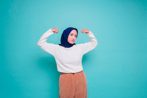 Excited Asian Muslim woman wearing a white shirt and hijab showing strong gesture by lifting her arms and muscles smiling proudly - Фото, изображение