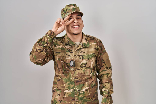 Young arab man wearing camouflage army uniform doing peace symbol with fingers over face, smiling cheerful showing victory  - Fotoğraf, Görsel