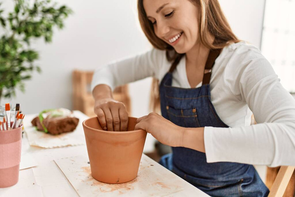 Young caucasian woman smiling confident make handmade clay pot at art studio - Photo, Image
