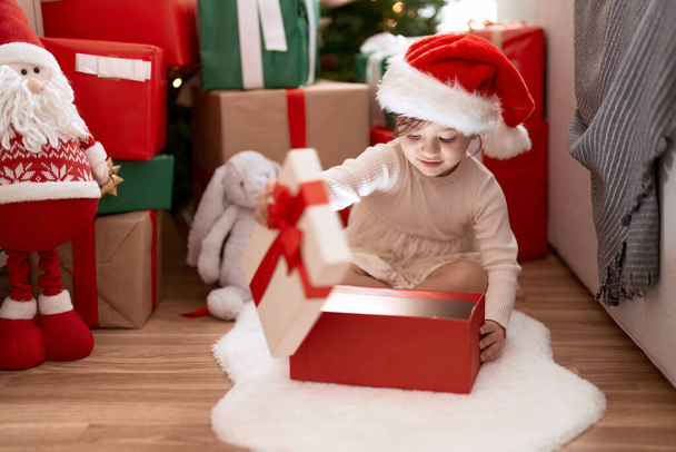 Sevimli kız hediyesini açıyor Noel ağacının yanında oturuyor. - Fotoğraf, Görsel