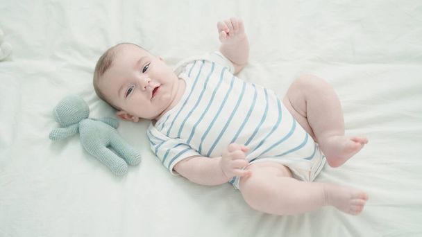 Adorable bebé caucásico sonriendo confiado acostado en la cama con en el dormitorio - Foto, imagen