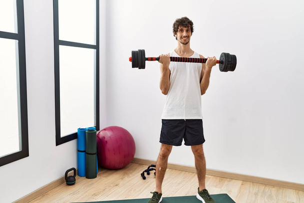 Young hispanic man smiling confident training using dumbbells at sport center - Foto, immagini