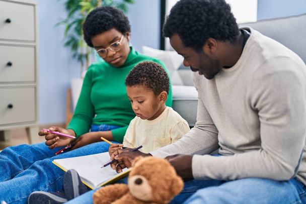 African american family drawing on notebook sitting on floor at home - Foto, immagini