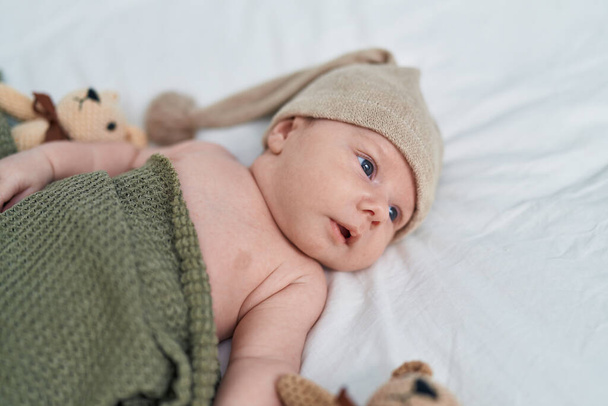 Adorable bebé caucásico acostado en la cama con expresión relajada en el dormitorio - Foto, Imagen