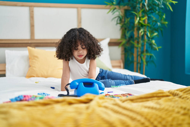 African american toddler playing with telephone toy sitting on bed at bedroom - Photo, Image