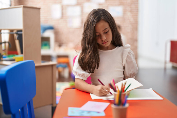 Adorable hispanic girl student sitting on table drawing on paper at kindergarten - Photo, Image