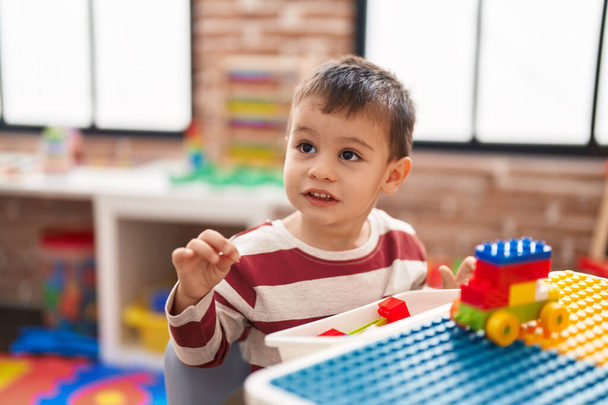 Красивый ребенок играет со строительными блоками, сидя на столе в детском саду - Фото, изображение
