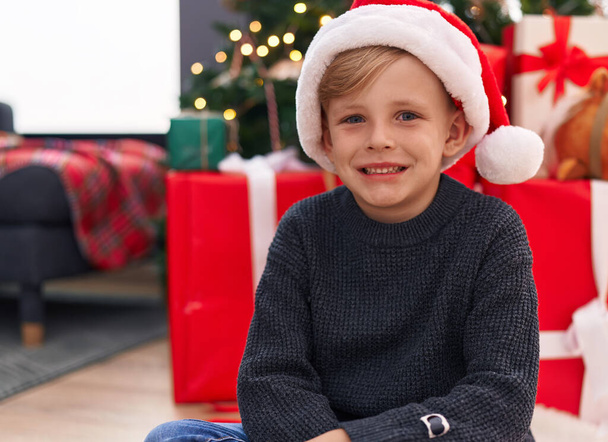 Rozkošné batole s úsměvem sebevědomí sedí na podlaze u vánočního stromku doma - Fotografie, Obrázek