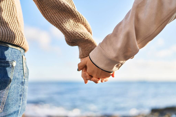 Мужская и женская пара стоят на заднем плане, рука об руку на берегу моря - Фото, изображение