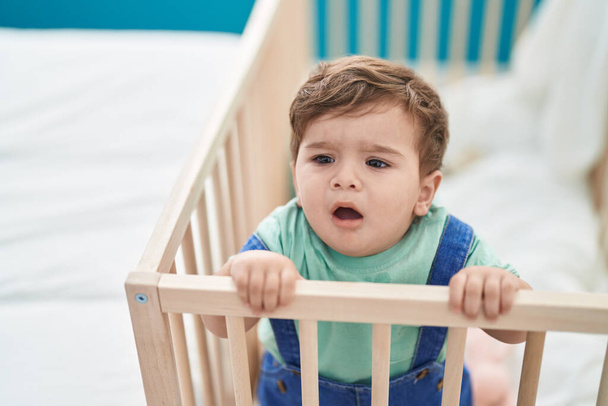 Adorable hispanic toddler standing on cradle crying at bedroom - Foto, afbeelding