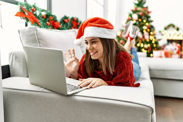 Genç İspanyol kız evdeki Noel ağacının yanında kanepede uzanmış video görüşmesi yapıyor.. - Fotoğraf, Görsel