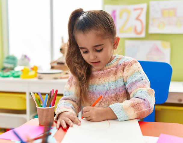 Adorable hispanic girl student sitting on table drawing on paper at kindergarten - Zdjęcie, obraz