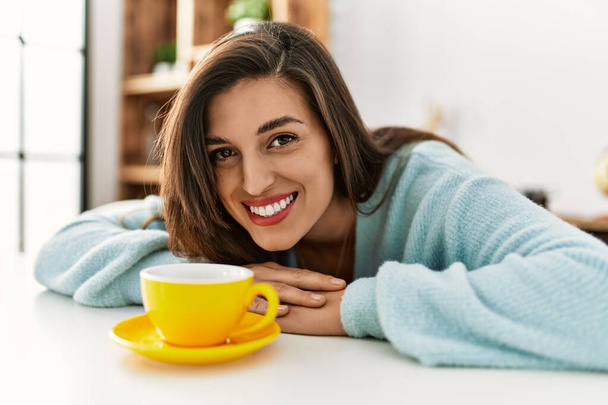 Молодая женщина пьет кофе сидя дома на столе - Фото, изображение