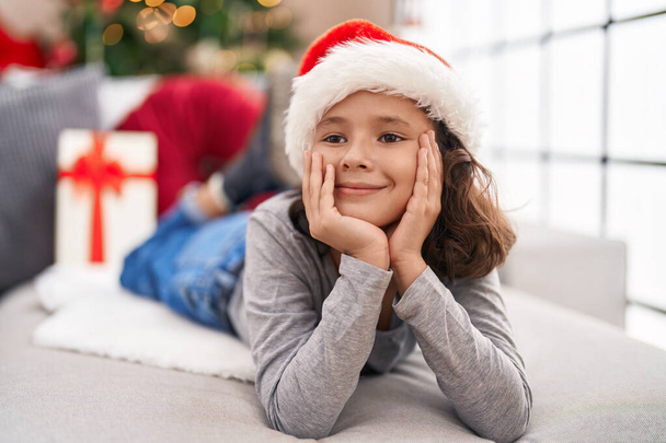 Adorable chica china sonriendo confiado acostado en el sofá por el árbol de Navidad en casa - Foto, imagen