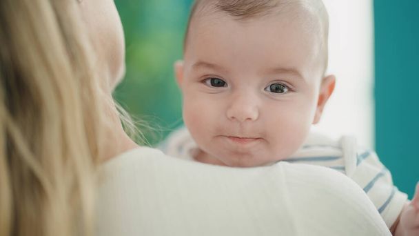 Чарівна біла дитина посміхається впевнено на материнських руках вдома
 - Фото, зображення