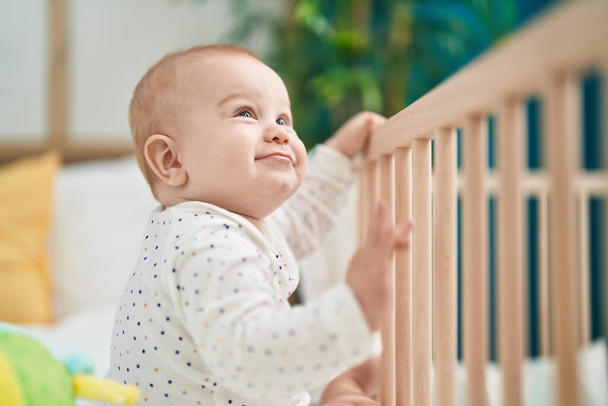 Imádnivaló kaukázusi baba mosolygós magabiztos álló bölcső a hálószobában - Fotó, kép