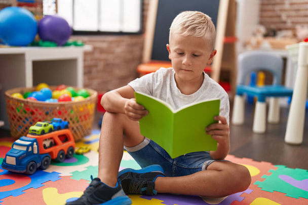 Adorable toddler student reading book sitting on floor at classroom - Photo, image
