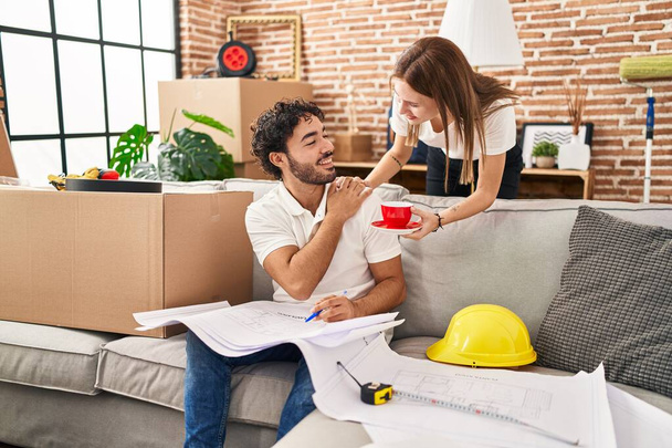 Man and woman couple drinking coffee looking house plans at new home - Foto, Imagem