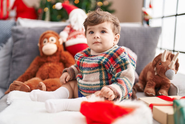 Adorable hispanic toddler sitting on sofa by christmas tree at home - 写真・画像