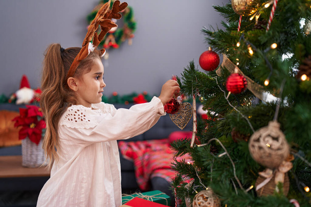 Entzückende hispanische Mädchen lächeln zuversichtlich schmücken Weihnachtsbaum zu Hause - Foto, Bild
