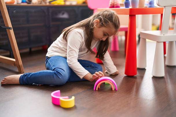 Чарівна іспаномовна дівчина грає з іграшками, сидячи на підлозі в дитячому садку
 - Фото, зображення