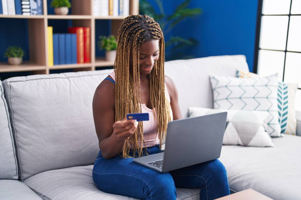 Donna afroamericana che utilizza laptop e carta di credito seduta sul divano di casa - Foto, immagini