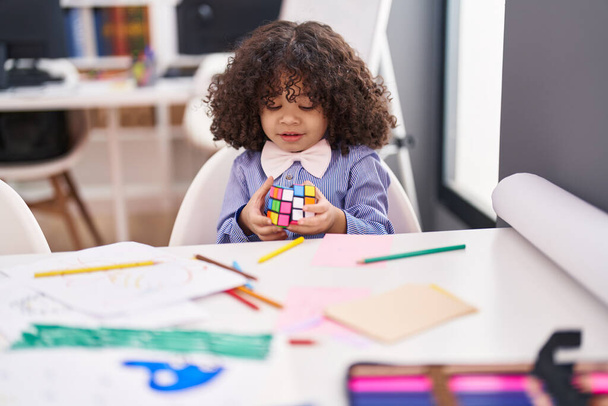 Afro-americano niño preescolar estudiante sentado en la mesa resolviendo cubo de Rubik en el jardín de infantes - Foto, Imagen