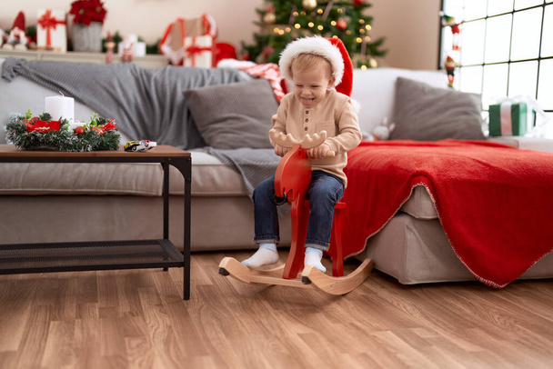 Adorable toddler smiling confident playing on reindeer rocking by christmas tree at home - Photo, Image