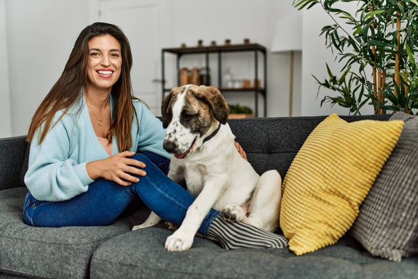 Giovane donna che abbraccia cane seduto sul divano a casa - Foto, immagini