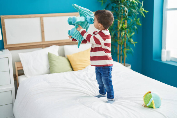 Adorável criança segurando elefante boneca de pé na cama no quarto - Foto, Imagem