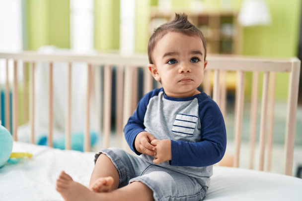 Sevimli İspanyol bebek yatak odasında rahat bir ifadeyle beşikte oturuyor. - Fotoğraf, Görsel