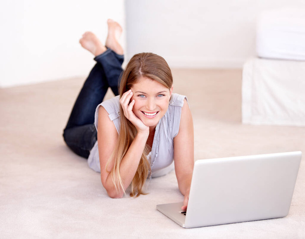 Modern living. A beautiful young woman using her laptop while lying on the floor - Foto, afbeelding