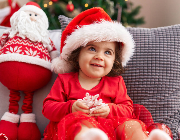 Adorable hispanic girl smiling confident sitting on sofa by christmas tree at home - Photo, Image