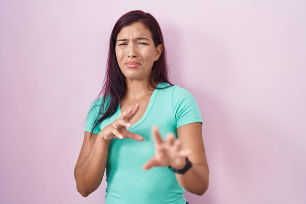 Young hispanic woman standing over pink background disgusted expression, displeased and fearful doing disgust face because aversion reaction.  - Photo, Image